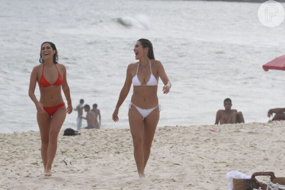 Flávia Alessandra e Fernanda Paes Leme gargalham ao andar na areia da praia do Recreio