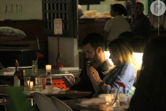 Gabriel Braga Nunes e Isabel Nascimento mexem no celular durante o jantar