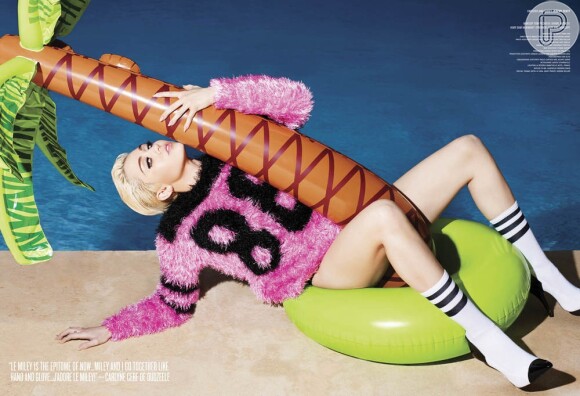 Em ensaio fotográfico, Miley usa apenas um casaco de cor rosa que contrapõe o cenário praiano