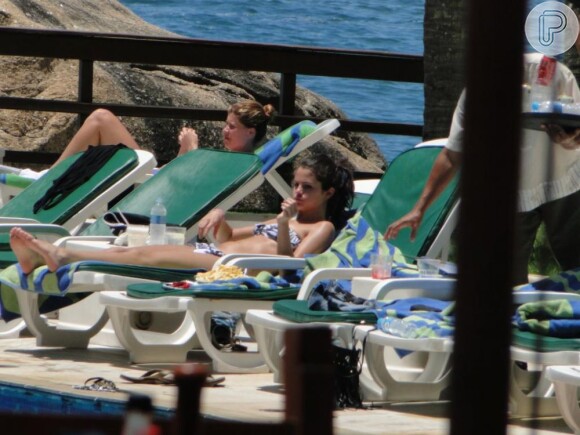 Selena Gomez tomando sol na piscina do hotel Sheraton, no Rio de Janeiro, acompanhada por algumas pessoas da produção do show. A cantora usa um biquini tomara que caia estampado