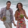Camila Pitanga e Gabriel Braga Nunes sorriem ao se aproximarem do mar, evitando molhar as roupas do figurino