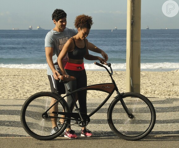 Dudu Azevedo segura a bicicleta para a colega de elenco