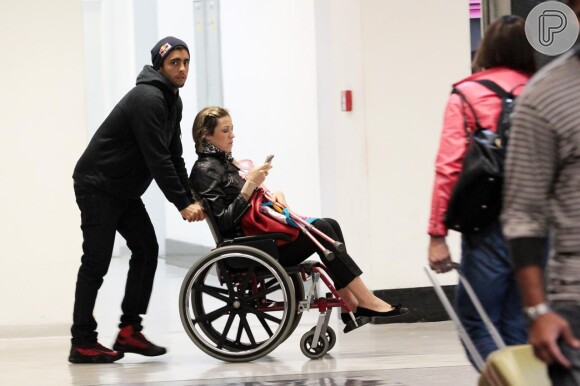 Logo após a cirurgia, Luana Piovani foi flagrada de cadeira de rodas no aeroporto, sendo empurrada pelo marido, Pedro Scooby