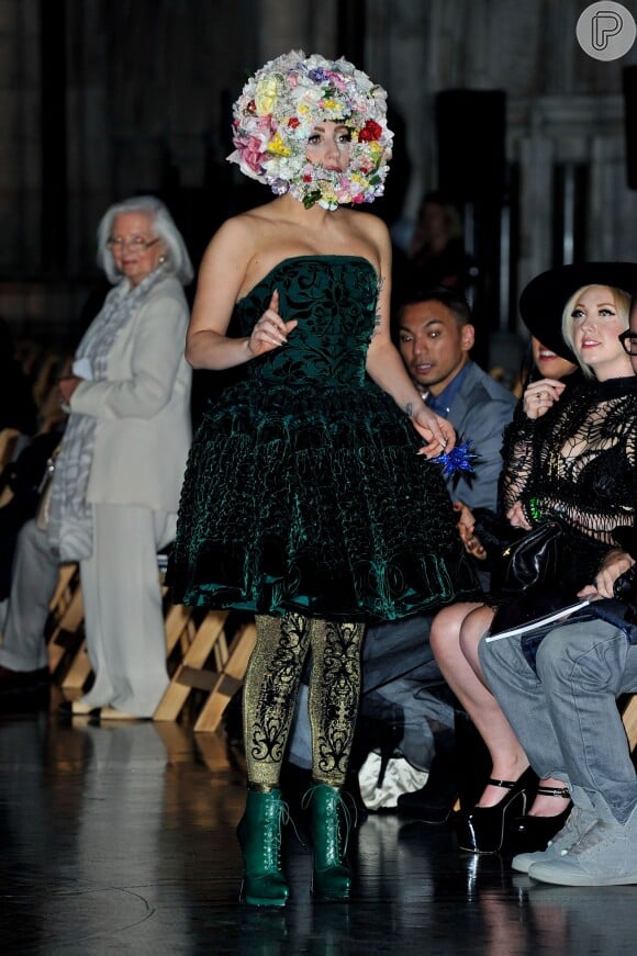 Lady Gaga não economizou em elementos conceituais para comparecer à edição de primavera/verão do London Fashion Week 2013. Ela escolheu botas de salto brilhantes e em verde oliva, como o vestido rodado, e uma meia calça com um tom mais claro da cor, com estampa tribal. Para fechar o look, nada como um adereço de flores, que cobriu até o queixo da cantora, no evento em Londres, que aconteceu em setembro de 2013