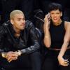 Chris Brown observa o jogo enquanto Rihanna faz cara feia falando no celular