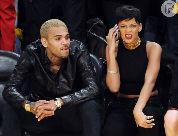 Chris Brown observa o jogo enquanto Rihanna faz cara feia falando no celular
