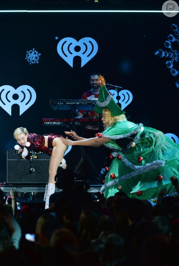 Miley Cyrus ao lado de dançarina vestida de árvore de Natal no tradicional show Jingle Ball Z100, no Madison Square Garden, em Nova York, no último sábado, 13 de dezembro de 2013