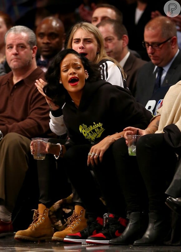Rihanna e Cara Delevingne riem durante partida de basquete