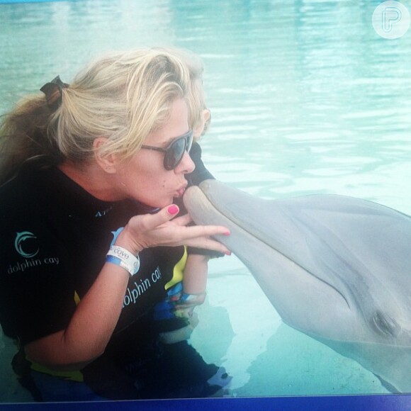 Adriane Galisteu beija golfinho em parque aquático nas Bahamas enquanto segura seu filho, Vittorio, de 2 anos, no colo, em 11 de janeiro de 2013