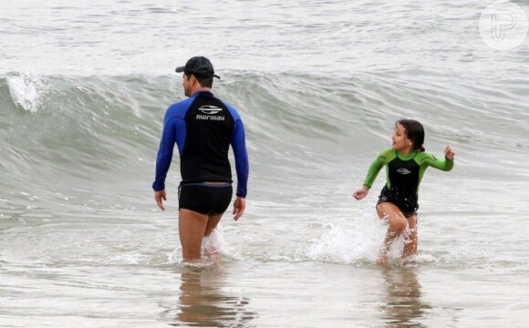 Catarina corre da onda, enquanto o pai se prepara para entrar novamente no mar