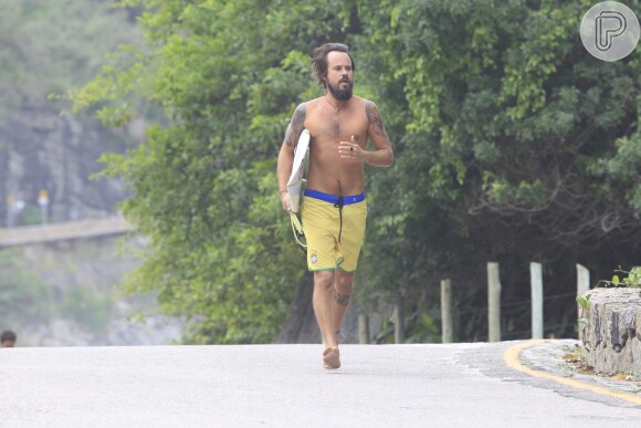 Paulinho Vilhena corre sem camisa segurando prancha de surfe