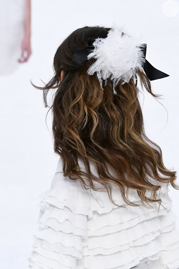 A presilha com tule e plumas brancas presa junto ao laço de fita preto foi destaque nos cabelos das modelos da Chanel