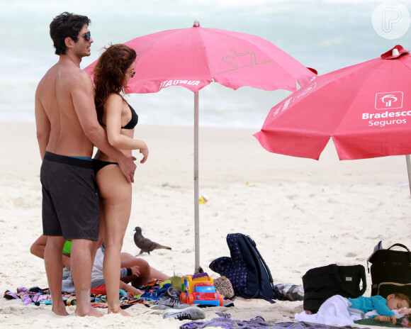 Isis Valverde e o marido, André Resende, observam o filho Rael tirar um cochilo na praia