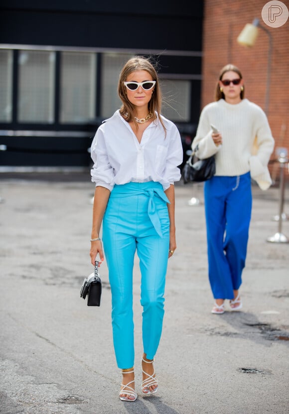 A calça azul vibrante pode ser combinada com camisa e sandálias brancas para um look de trabalho mais alto-astral e elegante no verão