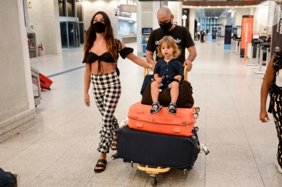 Filho de Isis Valverde deixa aeroporto sentado nas malas da família