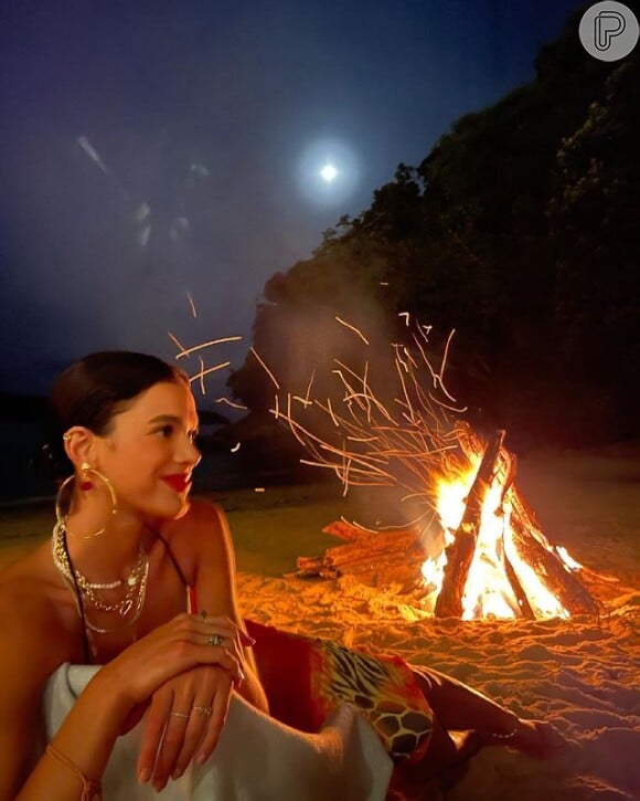 Bruna Marquezine posa em frente à fogueira com look com mais acessórios do que maquiagem