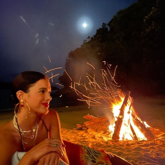 Bruna Marquezine posa em frente à fogueira com look com mais acessórios do que maquiagem