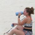 Larissa Manoela bebe água após exercícios na praia da Barra da Tijuca
