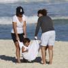 Em mais um dia de praia, Marcelo Sangalo se diverte ao ser balançado em uma toalha pela mãe e pela tia Cyntia