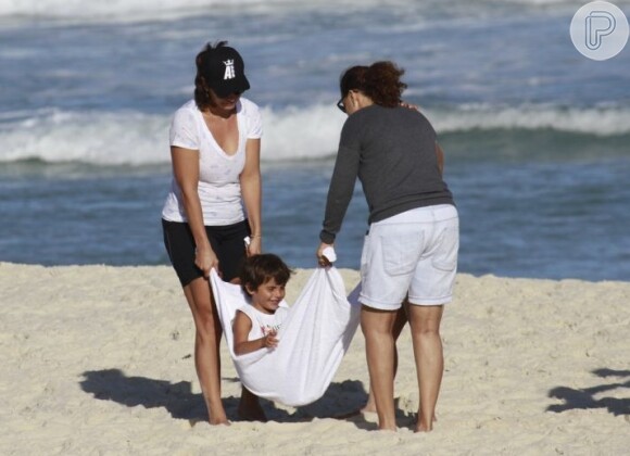 Em mais um dia de praia, Marcelo Sangalo se diverte ao ser balançado em uma toalha pela mãe e pela tia Cyntia