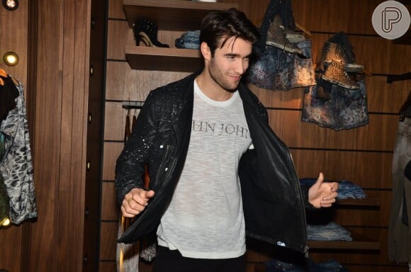 Joshua abre a jaqueta exibindo a camisa da marca por baixo e joga charme ao posar para fotos