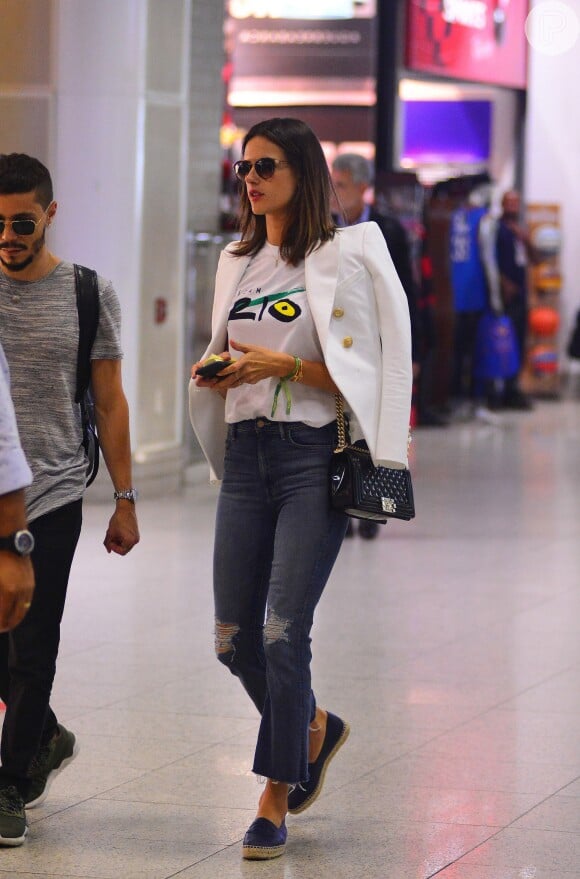 Alessandra Ambrosio passou por aeroporto usando calça pantacourt rasgada com camisa estampada e alpargata. Para dar elegância ao look, ela escolher blazer branco com detalhes dourados e bolsa Chanel