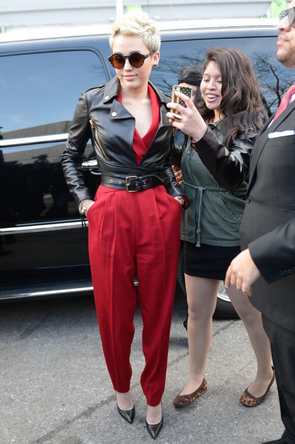 Miley Cyrus chega ao Fahion Show em Nova York, nos EUA, em 13 de fevereiro de 2013. Ela usa um macacão Rachel Zoe com uma jaqueta Moschino, óculos de sol Quay Eyeware Australia e sapatos Jean-Michel Cazabat