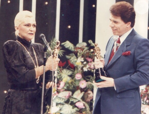 Silvio Santos (José Rubens Chachá) é surpreendido por Hebe Camargo (Martha Mellinger) na série 'O Rei da TV' em seu programa; na realidade, o dono do SBT chamou a apresentadora ao palco de sua atração em 21 de fevereiro de 1988