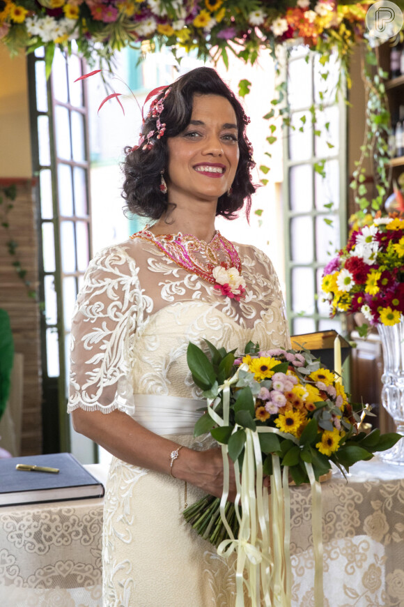 Verônica (Ana Cecília Costa) usa vestido com mangas e com um tule, com flores e detalhes rosas, além de um enfeite da mesma cor na cabeça