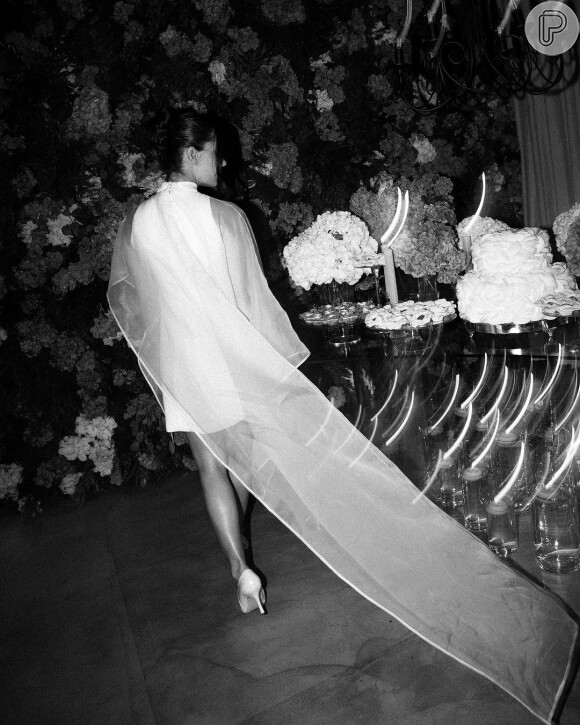 Jade Magalhães apostou em uma peça branca, minimalista e sofisticada, com gola alta, sem mangas e uma capa de organza de seda transparente para o casamento com Luan Santana. Em entrevista à CNN Brasil, Jade explicou: "Busquei algo atemporal, moderno e leve. Usamos organza de seda em um modelo assimétrico, de gola alta e com transparência".