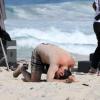Marcelo Adnet se agacha e coloca a cabeça na areia na praia de Ipanema, RJ