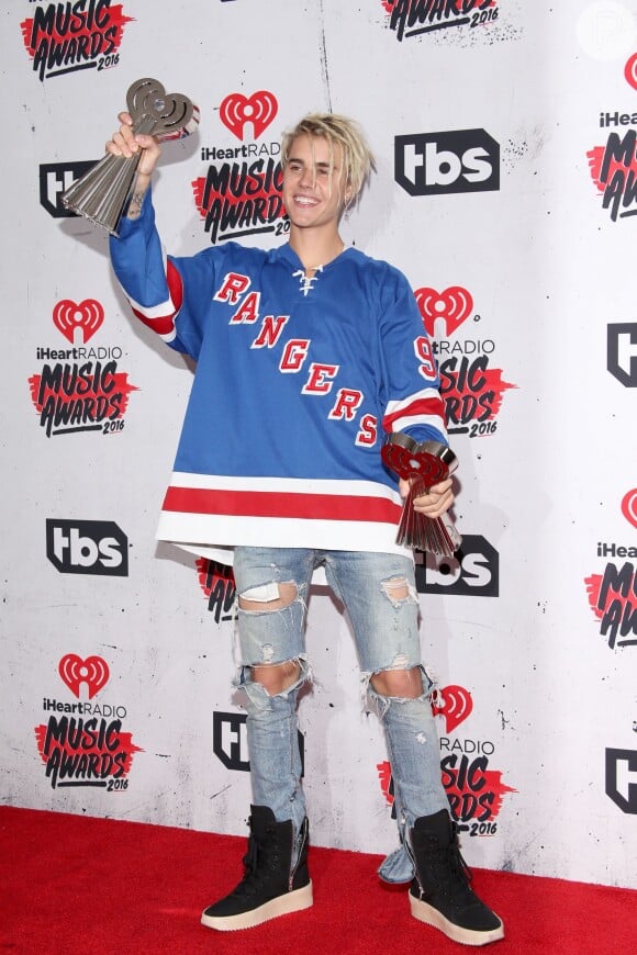 Justin Bieber apostou no street style para ir ao iHeartRadio Music Awards. O cantor usou calça jeans destroyed, blusa do time de futebol americano Rangers e tênis de cano alto