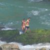 Cauã Reymond e namorada, Mariana Goldfarb, caminham sobre as pedras da praia
