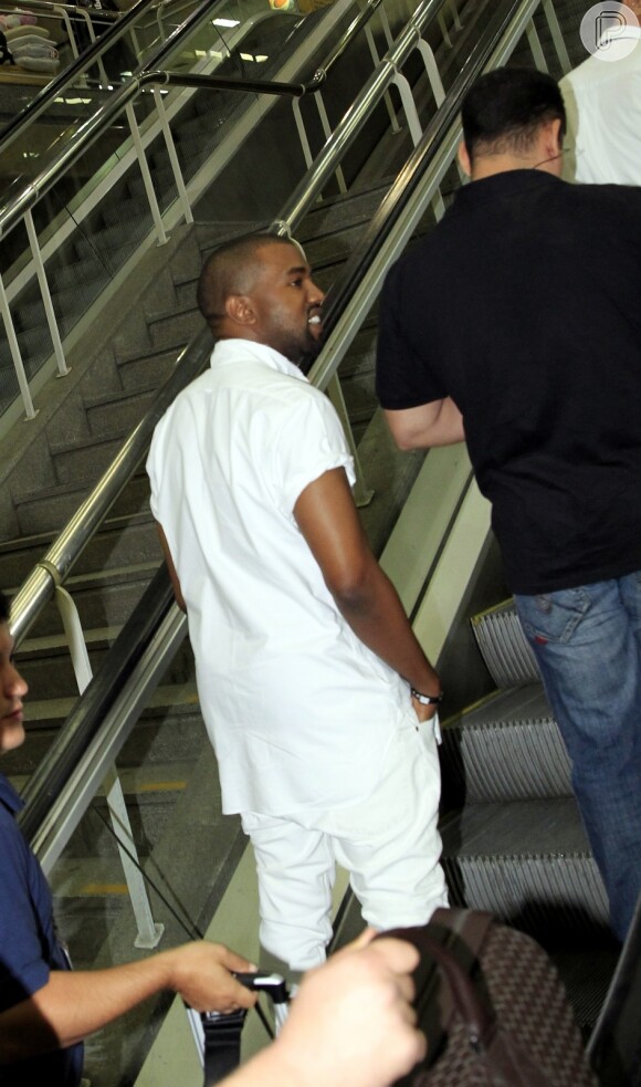 Kanye West esboça um sorriso ao subir a escada rolante