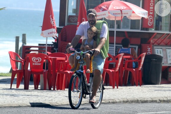 Thiago Lacerda chegou pedalando acompanhado pela filha na praia da Barra da Tijuca, no Rio
