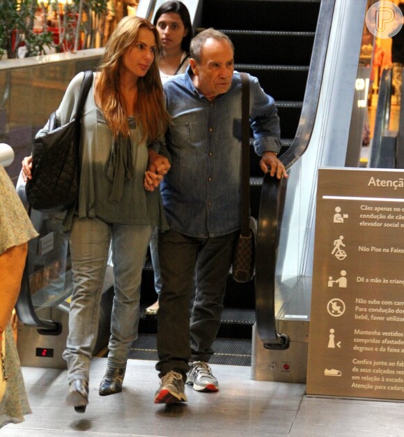 Stênio Garcia desce escada rolante juntinho com a mulher, Marilene Saade