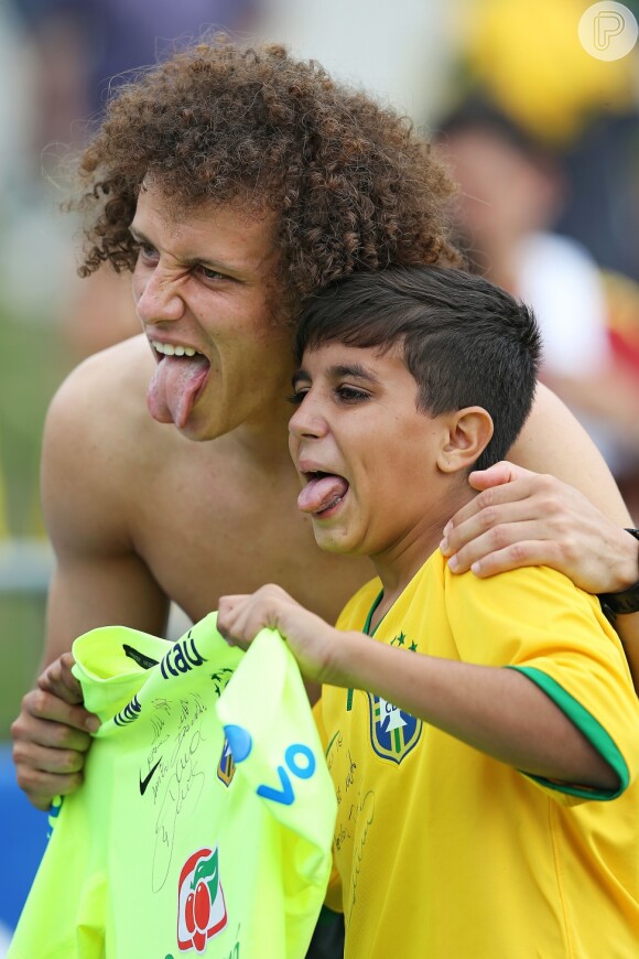 Brincalhão, David Luiz autografa a camisa de um fã mirim e posa fazendo careta ao lado dele