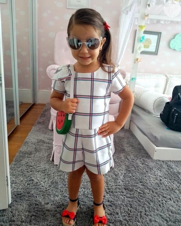 Maria Flor, filha de Deborah Secco e Hugo Moura, usou macaquinho xadrez com detalhe de lacinho na manga, óculos espelhados e bolsa de melancia