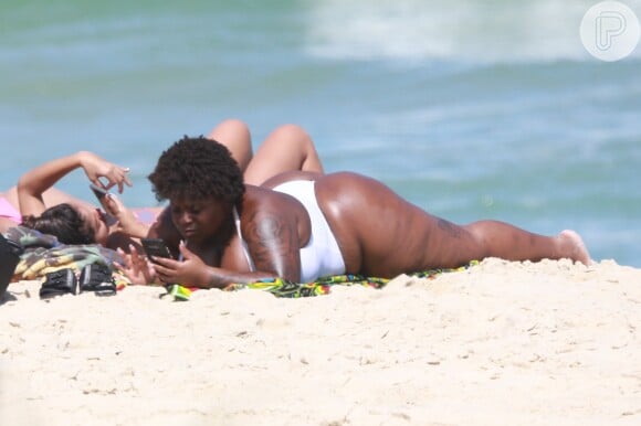 Anitta, de topless, mexe em celular em dia de praia com amigas