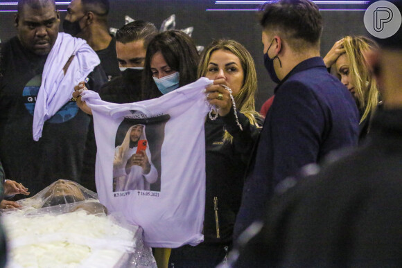 Viúva de MC Kevin, Adeolane Bezerra estende camisa com rosto do cantor estampado em funeral