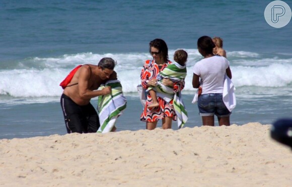 Cláudia Abreu veste a saída de praia e observa o marido enrolar a caçula Felpa