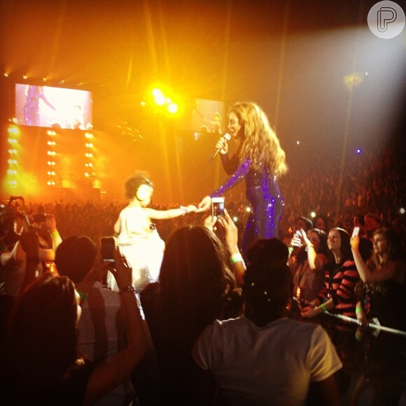 Beyoncé exibiu uma barriguinha saliente em show de Londres. Nesta foto, ela dá a mãe para a filha, Blue Ivy Carter, que estava na plateia