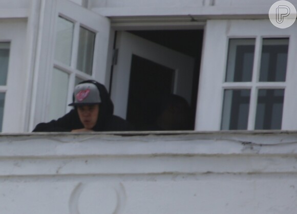 Justin Bieber de boné e casaco na sacada do hotel