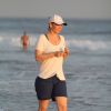 Julia Lemmertz usa bermudinha azul e camiseta branca para uma caminhada na areia
