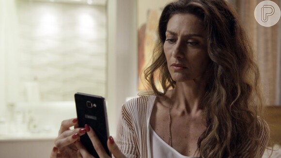 Joyce (Maria Fernanda Cândido) recebe uma foto de Irene (Débora Falabella) com Eugênio (Dan Stulbach), quando o marido não está em casa, na novela 'A Força do Querer'