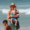 Karina Bacchi carrega o filho, Enrico, no colo durante tarde na praia da Barra