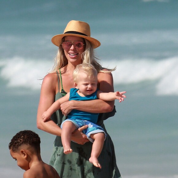 Karina Bacchi carrega o filho, Enrico, no colo durante tarde na praia da Barra