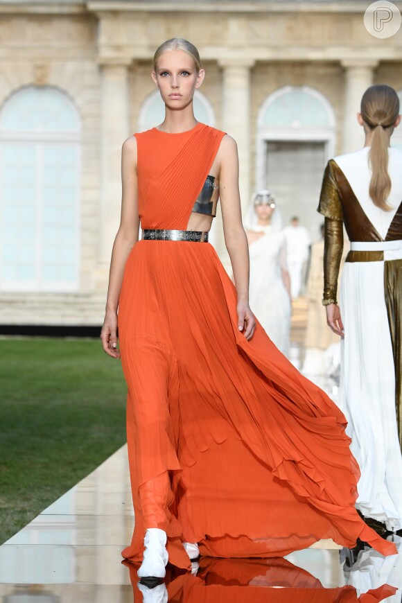 Laranja e assimetria no vestido da Givenchy; repare nas botas brancas