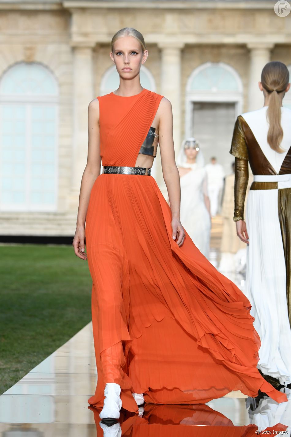 Laranja e assimetria no vestido da Givenchy; repare nas botas brancas