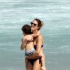 Leticia Birkheuer pega o filho, João Guilherme, no colo, em praia do Rio